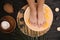 Woman soaking her feet in plate with water and orange slices on wooden floor, top view