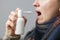 A woman with a sore throat sprays medicine aerosol spray down her throat