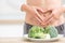 Woman with sports figure on her belly shows heart shape. Fresh broccoli in plate on kitchen table