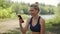 Woman in a sports top and wireless headphones communicates on phone smiling in nature. A young woman talks on the phone