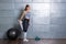 Woman in sports wear warming up before workout and stretching her leg in front of metal background and fitness equipment.