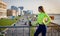 Woman in sportswear and a bottle of water stands on a bridge over a road with cars, buildings, sports girl in the city