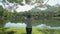 Woman in sportswear jogging and walking through the grass lawn under shade of the lush foliage trees to natural pond.