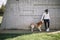 Woman in sportswear petting her dog while leaning on stone wall