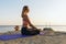 A woman in sportswear, practicing yoga, sitting on a mat in a lotus position, in the evening on the seashore
