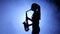Woman in spotlight in smoky studio plays on saxophone, silhouette