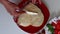 A woman is spreading cream on a biscuit. Next to the saucer is a strawberry and there is a cream.