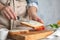 Woman spreading sauce on sandwich at light grey table, closeup