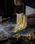 A woman sprinkles flour on a yellow paste on a dark table.