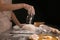 Woman sprinkling flour on dough against dark background