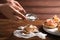 Woman sprinkling sugar powder on rose shaped apple pastry on wooden table