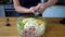 Woman squeezes garlic into a bowl of fresh vegetables and chicken salad. Preparing food in the home kitchen
