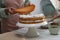 Woman stacking layers of sponge cake at white wooden table in kitchen, closeup