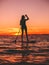 Woman stand up paddle boarding at dusk on a flat warm quiet sea with beautiful sunset