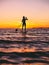 Woman stand up paddle boarding at dusk on a flat warm quiet sea with beautiful sunset colors