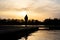 Woman standing alone at sunset on end of lake pier jetty thoughtful calm river below. Golden sunrise summer sun light reflection