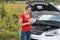 Woman standing at broken car in meadow and reading owner manual