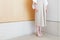 Woman standing in corner beige dress with mid heel shoe minimal style.