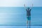 Woman standing on edge of swimming pool with raised hands over head, she looking at seascape view.