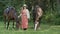 Woman standing between horses grazing on green meadow