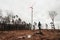 Woman standing and looking on  wind turbine station in destroyed and deforested forest on tree stump in bad weather conditions -