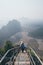 Woman standing on mountain peak with stairs going down during sunrise foggy morning in Hpa-An, Myanmar