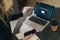 Woman standing near table,pointing pencil on laptop with inscription on screen e-learning, image of square academic cap