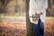 Woman standing near the tree and holding seasonal bouquet in her hands on a sunny autumn day in the park. Girl walking