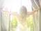 Woman standing near the window which  stretching near bed after waking up with sunrise at morning and lens flare