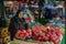 a woman standing at an open market selling tomatoes