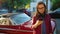 Woman is standing outdoors near the red vintage car and using smartphone