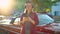 Woman is standing outdoors near the red vintage car and using smartphone