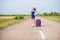 A woman is standing on the road with a hat and with a big bag. Girl in a blue tight-fitting dress with a purple suitcase