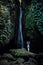 Woman standing on the rock, practicing yoga. Young woman raising arms with namaste mudra near waterfall. Leke Leke waterfall, Bali