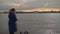 A woman is standing on the shore and feeding gulls. Evening time