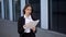 A woman is standing on the street near the building looking through documents.