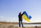 woman stands against the background of the lake and holds the Ukrainian yellow-blue flag against the sky