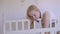 A woman stands at a baby crib and admires her little sleeping baby