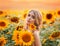 woman stands in a field with blooming sunflowers and hugs a bouquet of flowers