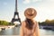 A woman stands in front of the iconic Eiffel Tower in Paris, France, tourist woman in summer dress and hat standing on beautiful