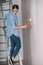 Woman stands on a ladder to paint her walls white