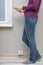 a woman stands near a socket with a phone in her hand that is charging