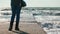 A woman stands on the pier, washed by the waves of the ocean. In the background, a seagull. Slow motion