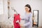 Woman is steaming red dress in room. She holds small stream iron in hand