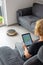 Woman is steering her vacuum cleaning robot from the sofa