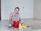 A woman stirs glue in a red bucket for wallpapering in an apartment.