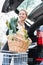 Woman storing basket with groceries into trunk after shopping