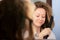 Woman straightens her hair with an iron in front of a mirror