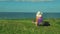 A woman in a straw hat with a backpack behind her back sits on a mountain and admires the view below. shooting from the back.