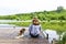 Woman with straw hat while sitting on the pier with her puppy and admiring the landscape